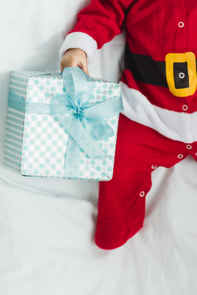 recortado tiro de pequeño bebé en traje de santa acostado en cuna con regalo de Navidad
 - Foto, Imagen