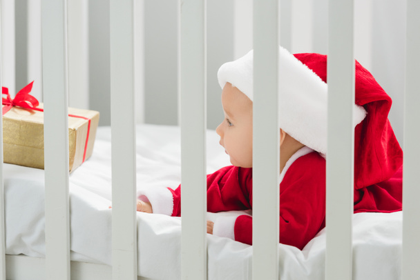 adorable bebé en traje de santa acostado en cuna con regalo de Navidad
 - Foto, Imagen