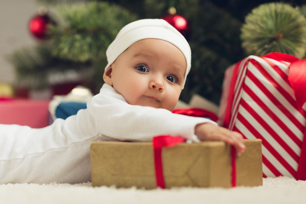 Detailní portrét rozkošné miminko leží na podlaze s vánoční dárky a při pohledu na fotoaparát - Fotografie, Obrázek