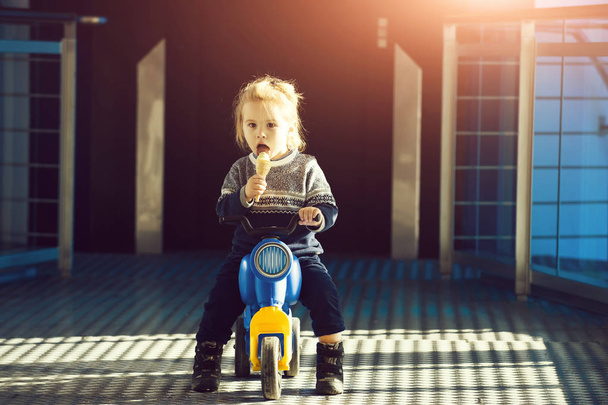 portrait of cute small boy eating ice cream, playing and sitting on toy bike on road sunny outdoor, activities at childhood and education concept - Fotoğraf, Görsel