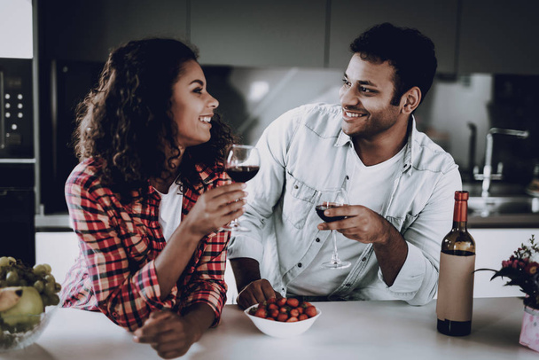 Afro American Couple Drinking Wine On In Kitchen. Weekend Concept. Family Holiday Resting. Romantic Date. Cheerful Sweethearts. Glass Of Wine. Happy Together. Looking At Each Other. - Zdjęcie, obraz