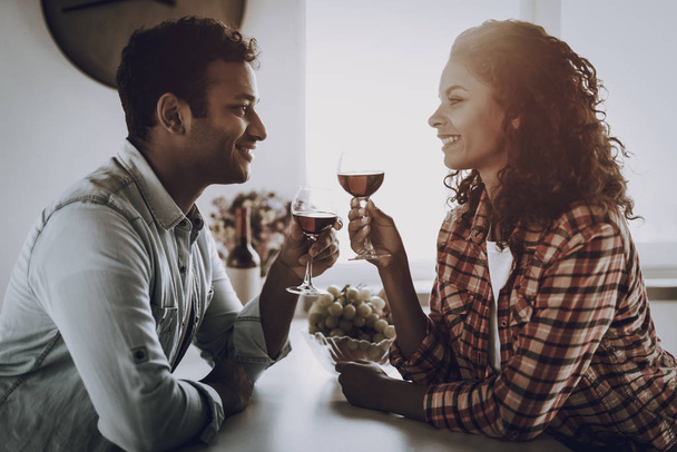 Afro American Couple Drinking Wine On In Kitchen. Weekend Concept. Family Holiday Resting. Romantic Date. Cheerful Sweethearts. Glass Of Wine. Happy Together. Looking At Each Other. - Фото, изображение