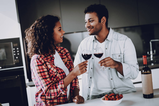 Afro American Couple Drinking Wine On In Kitchen. Weekend Concept. Family Holiday Resting. Romantic Date. Cheerful Sweethearts. Glass Of Wine. Happy Together. Looking At Each Other. - 写真・画像