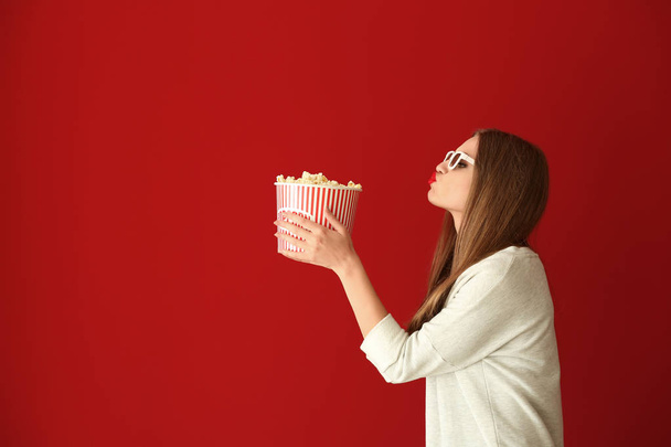 Beautiful young woman with cup of popcorn and 3D cinema glasses on color background - Photo, Image