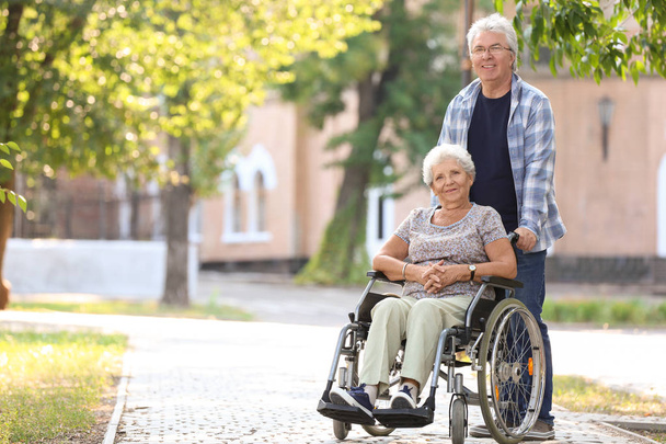 Mujer mayor en silla de ruedas y su marido al aire libre
 - Foto, imagen