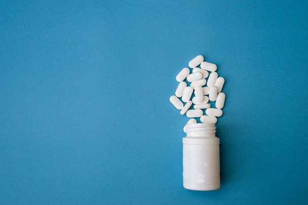 medicamento comprimidos blancos y frasco de medicamento aislado sobre fondo azul. Vista superior
 - Foto, Imagen