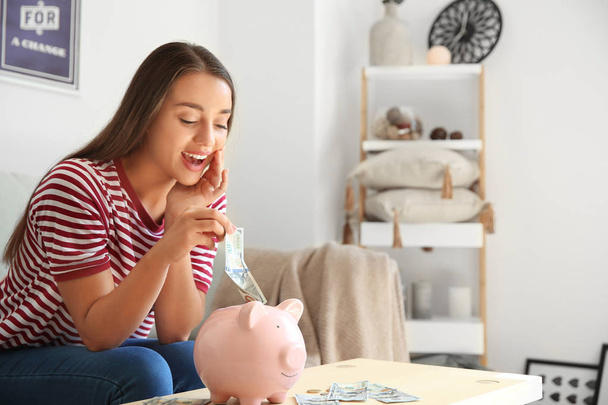 Young woman with piggy bank at home - Φωτογραφία, εικόνα