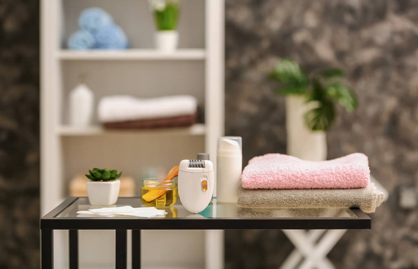 Modern epilator, sugaring paste and towels on table in beauty salon - Photo, Image