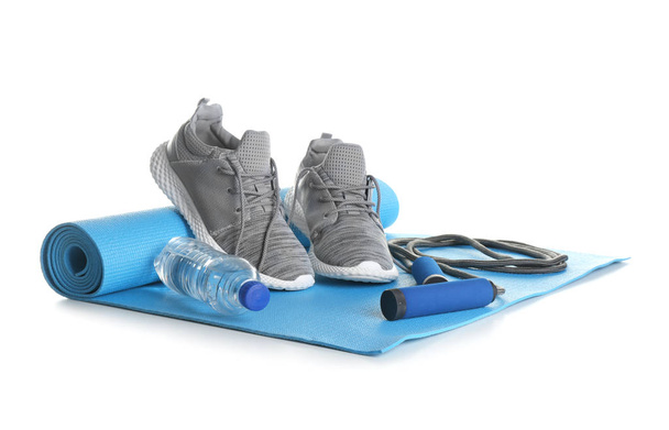 Yoga mat met sportschoenen, touw en fles water springen op witte achtergrond - Foto, afbeelding