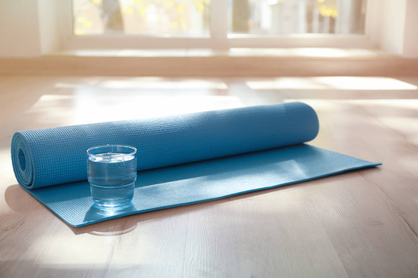 Yoga mat and glass of water on floor indoors - Photo, Image