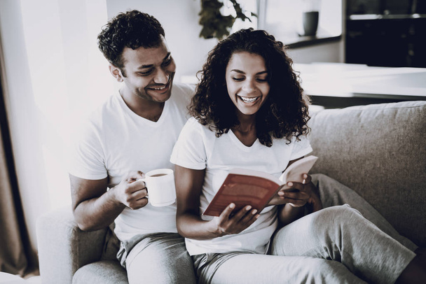 Man With Cup Of Coffee. Girlfriend Reads On Couch. Morning Leisure. Have A Break. Home Clothes. Holiday Resting. Smiling Together. Happy Young Afro American Couple. Cup Of Coffee. Love Each Other. - Foto, Imagen