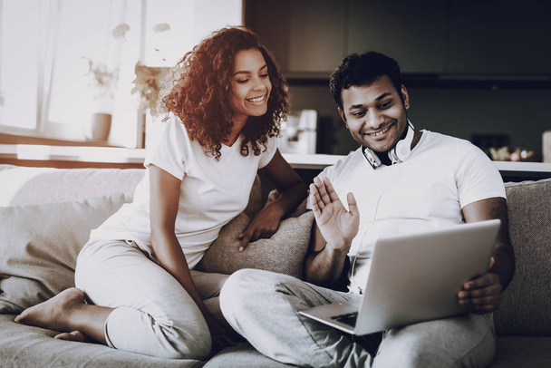 Afro American Couple Greeting On Laptop Camera. Staring On Screen. Happy Together. Morning Leisure. Chilling On Sofa. Home Clothes. Holiday Resting. Smiling Communication. Chat With Someone. - Фото, изображение