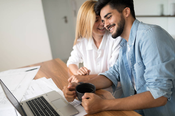 Photo of cheerful loving young couple using laptop and analyzing their finances with documents - Photo, image