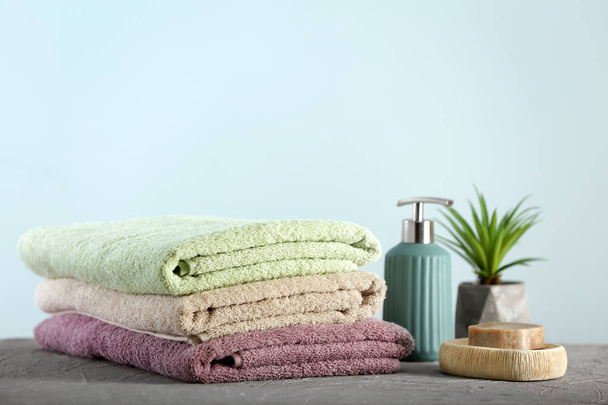 Clean folded towels and bath cosmetics on table against light background - Photo, Image