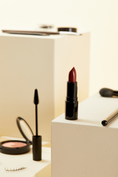 close-up shot of red lipstick with various makeup accessories on beige cubes - Foto, afbeelding