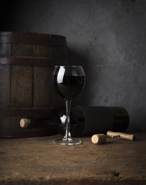 Excellent red wine bottles, wineglass, barrel and corkscrew on a rustic wooden table: traditional winemaking and wine tasting concept - Photo, Image