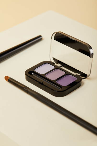 close-up shot of purple eyeshadows case with brush on beige - Foto, imagen