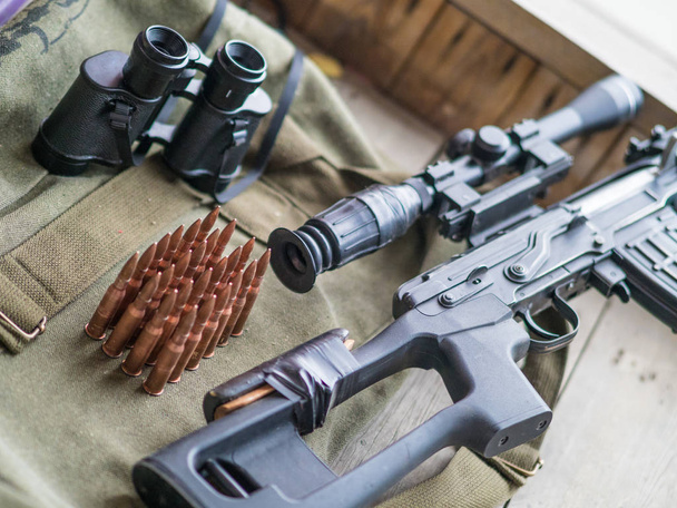 Sniper rifle, binoculars and ammo laying on a wooden floor - Photo, Image