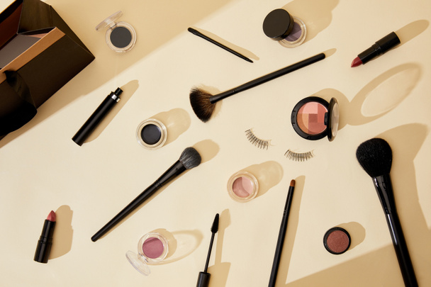 top view of different cosmetics and false eyelashes lying on beige tabletop - Photo, Image