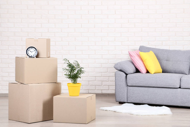 Cardboard boxes with household stuff and grey sofa on brick wall background - Zdjęcie, obraz