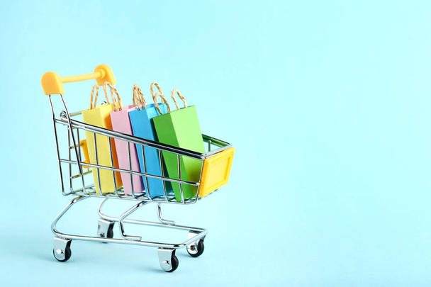 Small paper shopping bags with shopping cart on blue background - Foto, Imagem