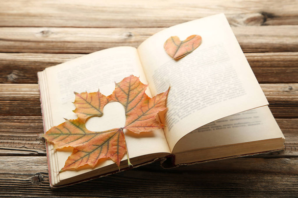 Dry maple leaf with heart and open book on brown wooden table - 写真・画像