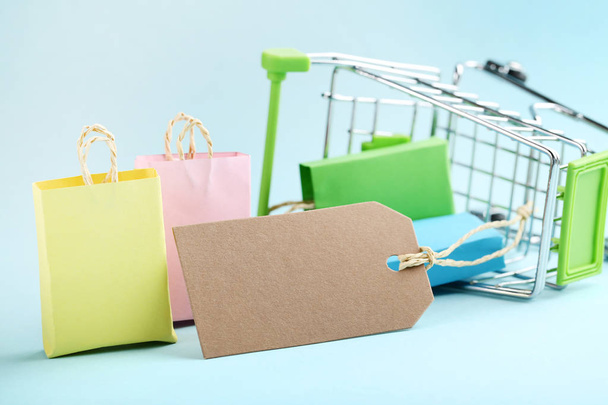 Small paper shopping bags with upturned shopping cart on blue background - Фото, изображение