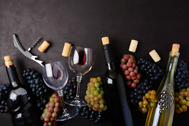 Wineglasses with red and white wine, bottles, grapes, corkscrew and corks lying on dark wooden background. Top view. Flat lay. Copy space - Fotoğraf, Görsel