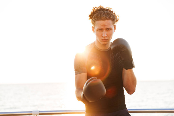 Focused young sportsman in boxing gloves training outdoors - Foto, immagini