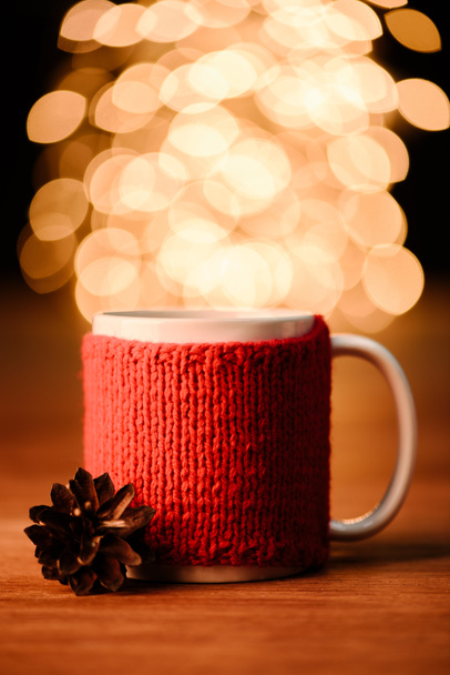 Nahaufnahme der Tasse Heißgetränk und Tannenzapfen auf Holztischplatte mit Bokeh-Licht Hintergrund - Foto, Bild