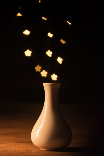 close up view of white vase and yellow stars bokeh lights on black background - Photo, image