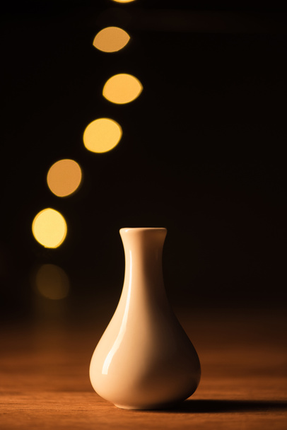 close up view of white vase and yellow bokeh lights on black background - Φωτογραφία, εικόνα
