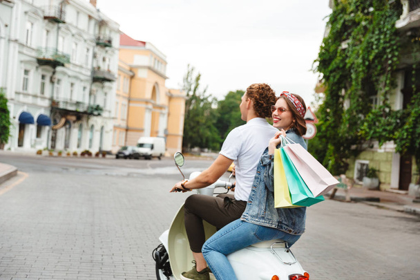 Back view of young lovely couple riding on the retro scooter with packages outdoors - Fotografie, Obrázek