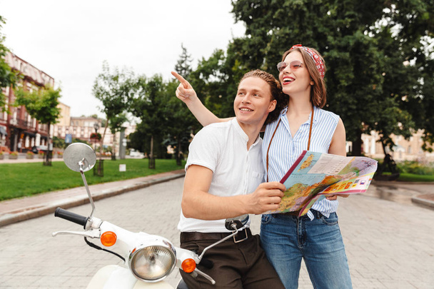 Happy young couple standing together with motorbike at the city street, analyzing city guide map - Foto, Imagen