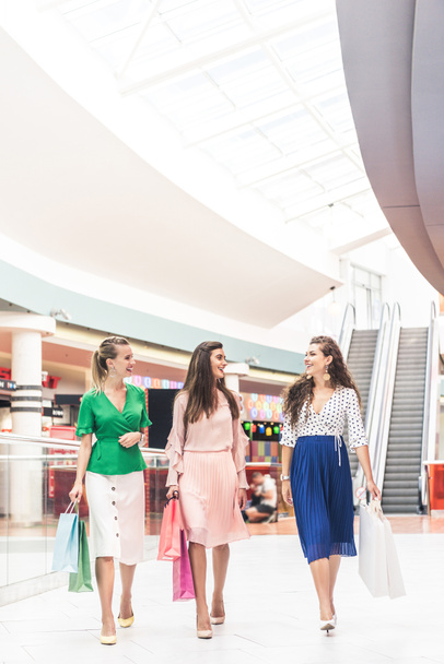beautiful smiling young women holding paper bags and talking while walking together in shopping mall - Foto, immagini