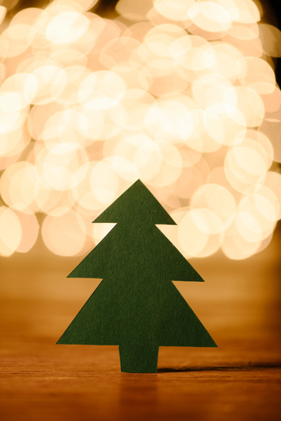 close up view of green paper christmas tree on wooden tabletop and bokeh lights background - Foto, Imagem
