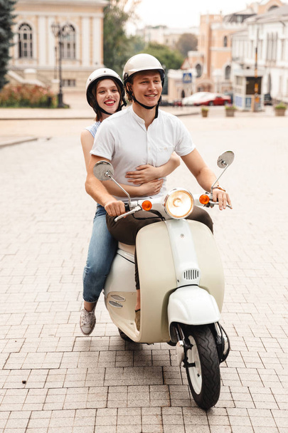 Portrait of a happy young couple in helmets riding on a motorbike together at the city street - Zdjęcie, obraz