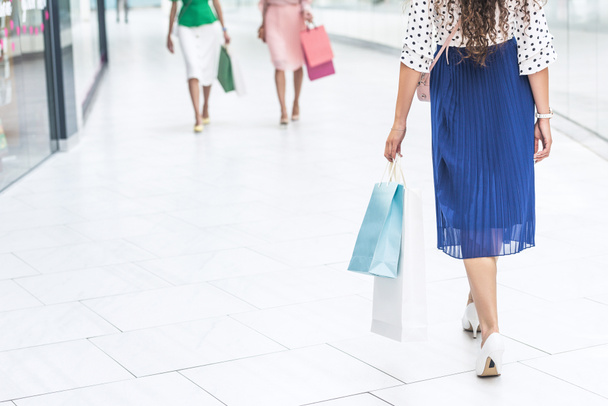 low section of stylish girls in skirts and high heeled shoes walking with shopping bags in mall - Photo, Image