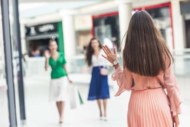 back view of young woman greeting female friends while walking in shopping mall - Foto, Bild