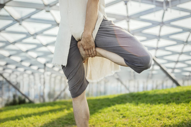 Close up of attractive athletic man practicing yoga and warming up in modern park at green grass outdoors. - Foto, immagini