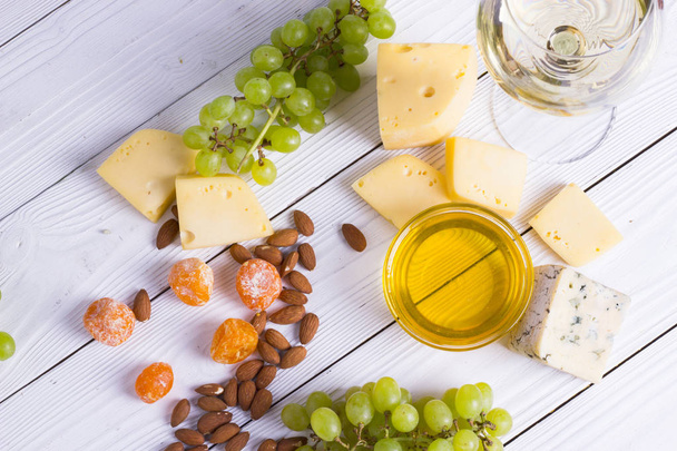 Glass of white wine with snacks - various types of cheese, figs, nuts, honey, grapes on a wooden boards background. Top view - Foto, Imagem