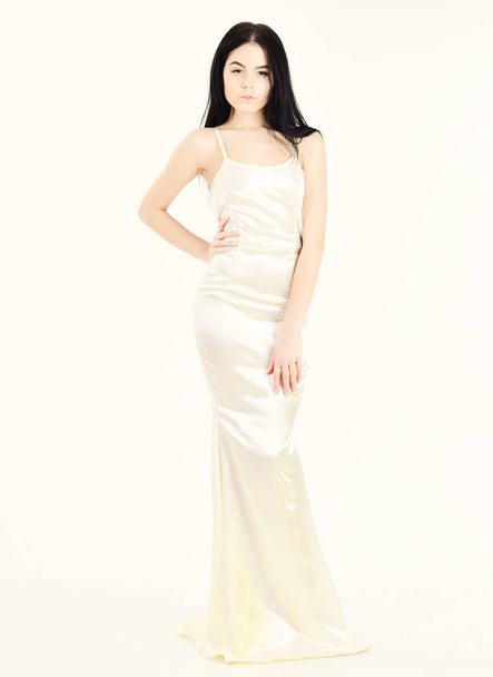 Femininity concept. Fashion model wears expensive fashionable evening dress or wedding dress. Girl on pensive face in graceful dress. Woman in elegant white dress with long hair, white background - Fotó, kép