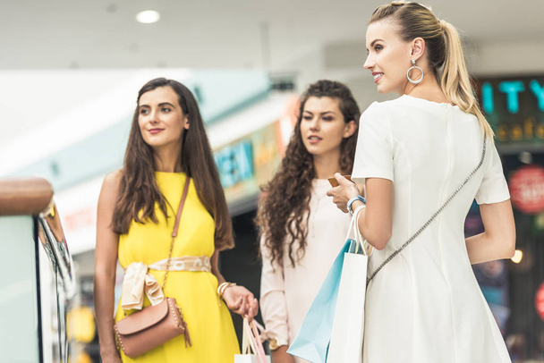 hermosas mujeres jóvenes de moda sosteniendo bolsas de papel y mirando hacia el centro comercial
 - Foto, imagen