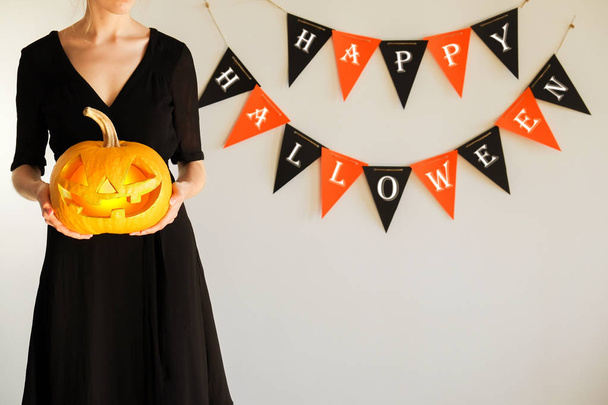 Portrait of young skinny woman in black dress, holding Jack O Lantern pumpkin against in hands. All hallows eve Halloween party concept. Traditional decoration. Close up, copy space, background - Foto, Imagem