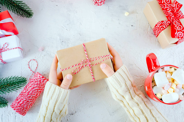 Kind hält Weihnachtsgeschenkbox mit einem roten Band gebunden, rote Tasse Kakao mit Marshmallow auf weißem Hintergrund. Weihnachtskarte Urlaubskonzept, Kopierraum - Foto, Bild