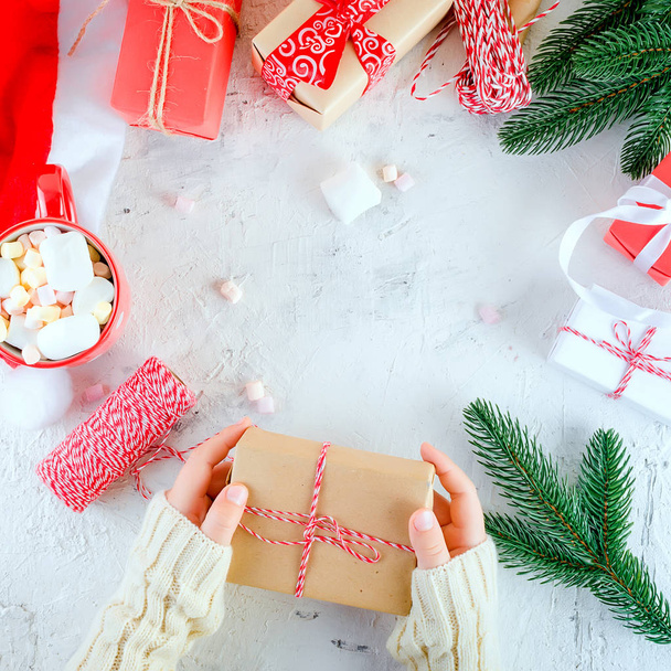 το παιδί κρατάει Χριστούγεννα δώρο κουτί δεμένο με μια κόκκινη κορδέλα, κόκκινο φλιτζάνι κακάο με marshmallow για το λευκό φόντο. Χριστουγεννιάτικη κάρτα διακοπών ιδέα, αντίγραφο χώρου - Φωτογραφία, εικόνα