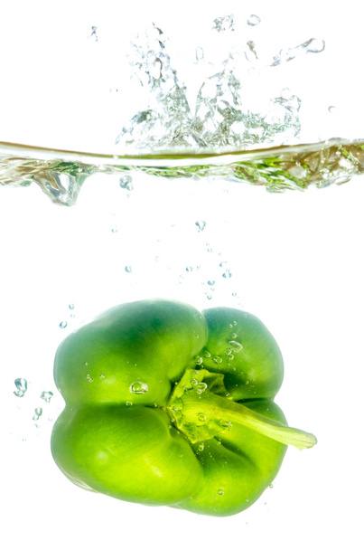 green paprika pepper splashes into water before white - Foto, afbeelding
