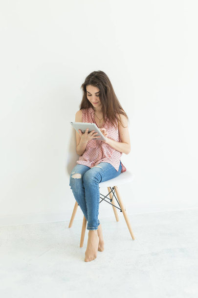 Sandalyede oturuyor ve dijital tablet izlerken veya beyaz zemin üzerine internette sörf genç kadın - Fotoğraf, Görsel