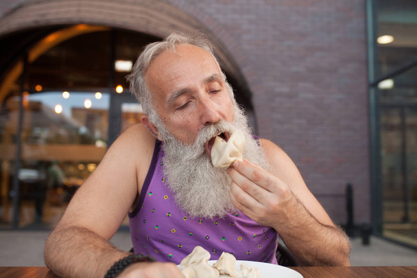 Senior Man eating in georgian restaurant national snack Khinkali, that is a relative to dumplings and raviolli - Foto, immagini