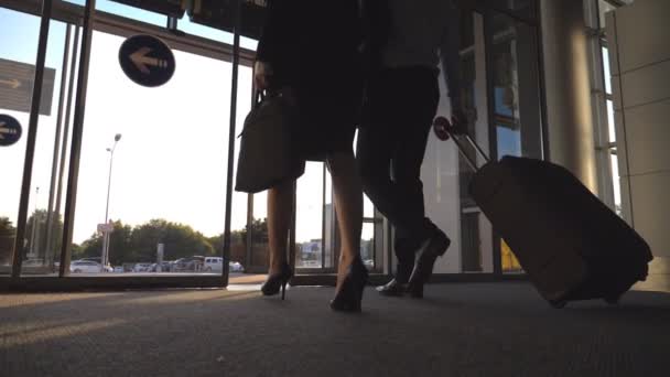 Бизнесмен со своей коллегой покидает терминал через стеклянные двери и катает чемодан на колесах. Бизнесмен и женщина едут из аэропорта на городскую улицу со своим багажом. Медленное движение
 - Кадры, видео